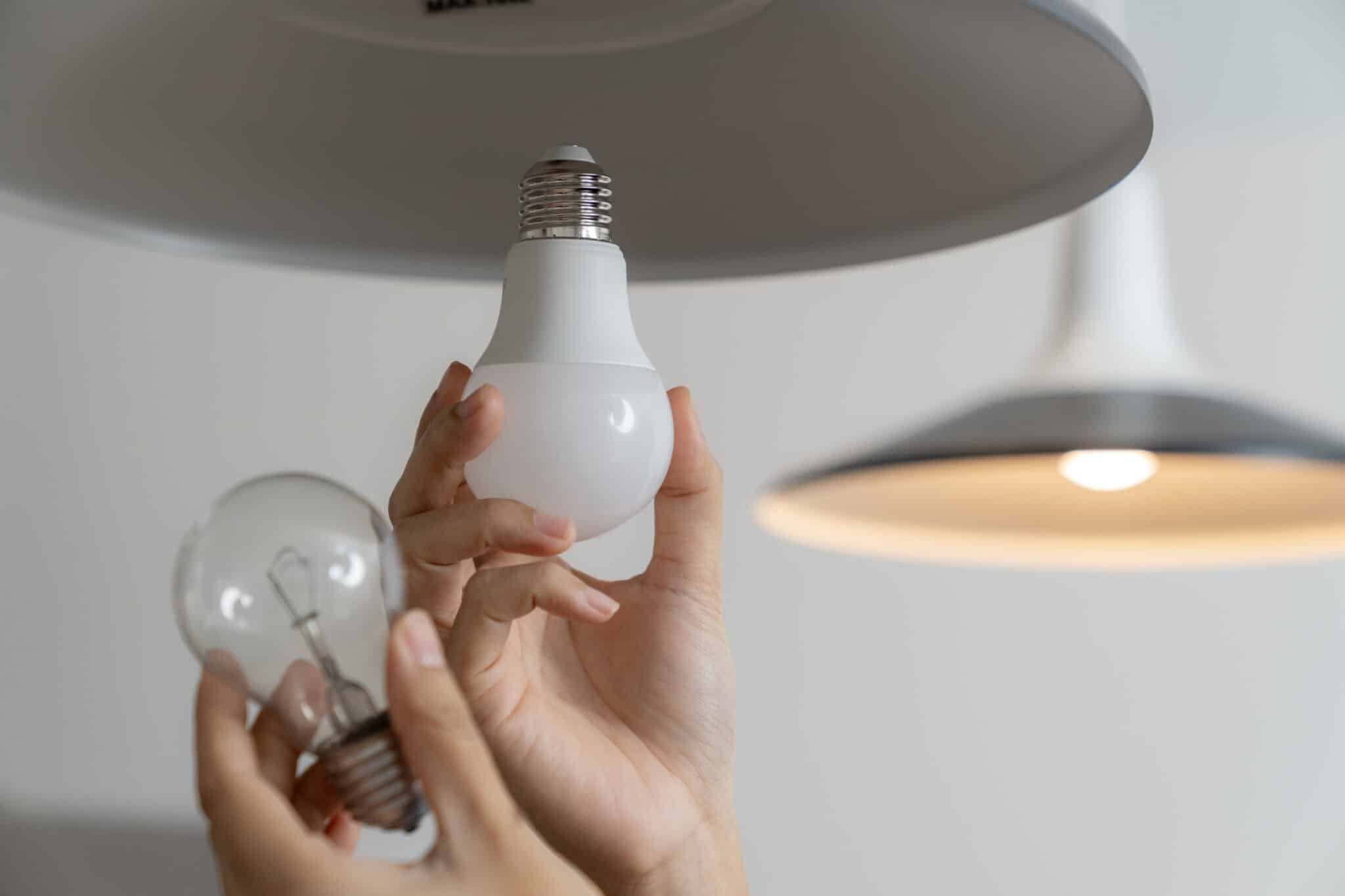 A woman replacing an incandescent light bulb with an LED light bulb.